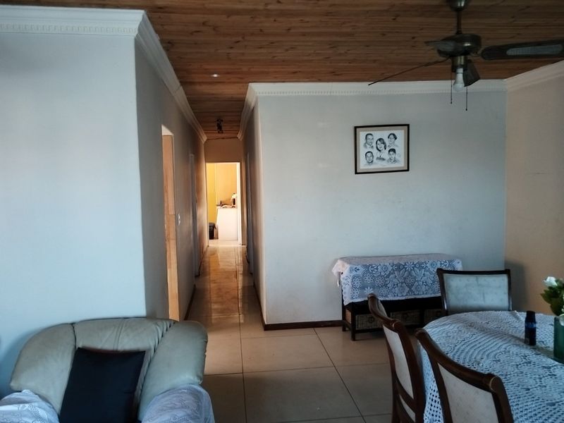 A living area featuring tiled flooring, a timber ceiling with a central fan, and a hallway leading to other parts of the home.