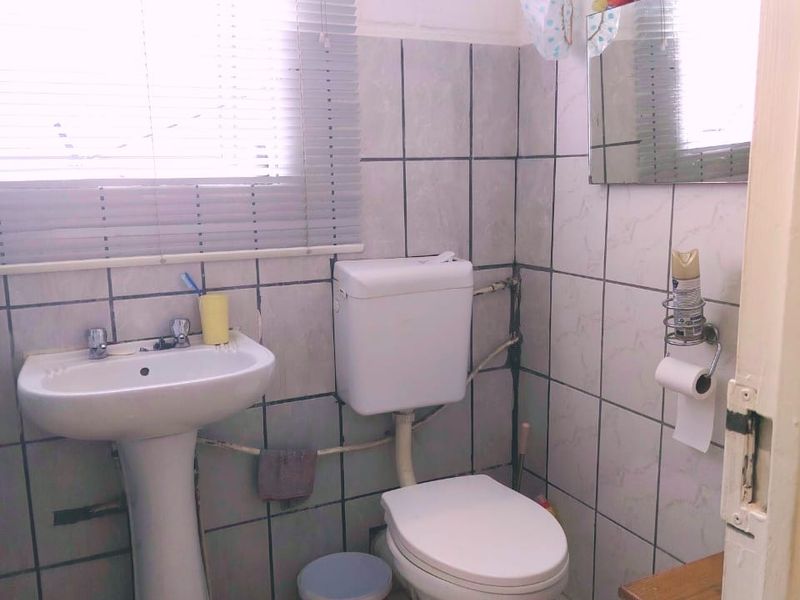 A compact bathroom featuring a pedestal basin, toilet, and tiled finishes, requiring some cosmetic updates and maintenance to the exposed plumbing and wall surfaces.