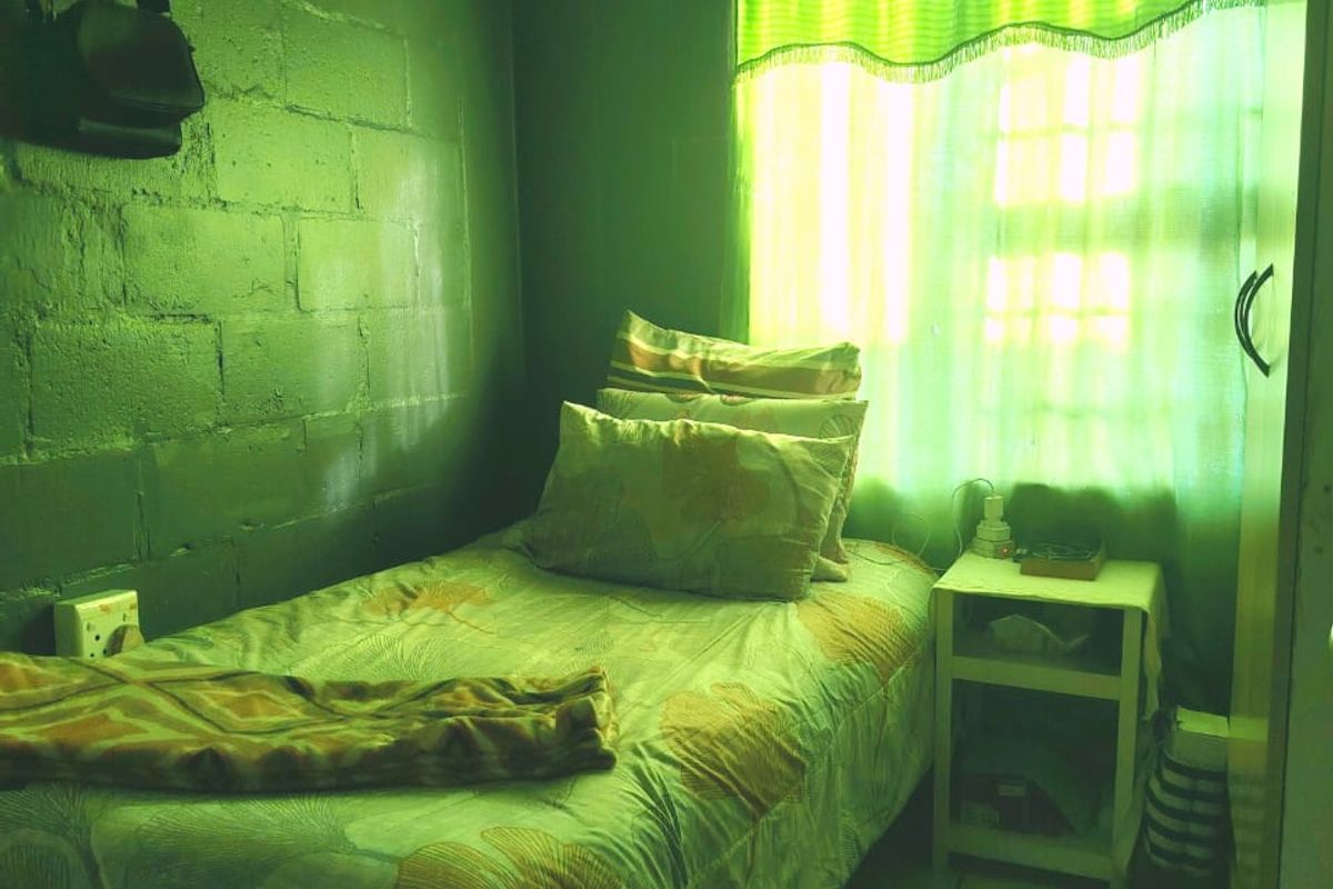A compact bedroom featuring tiled flooring and an exposed blockwork wall, currently finished with a strong green lighting cast.