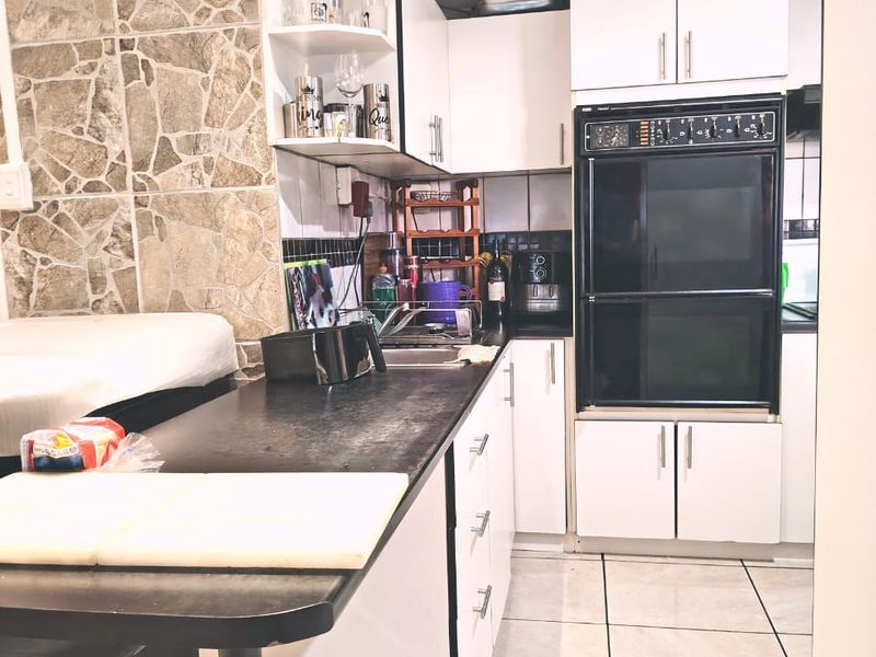 Compact kitchen featuring white cabinetry, built-in oven, dark laminate countertops, and a distinctive stone-cladding feature wall with tiled flooring.