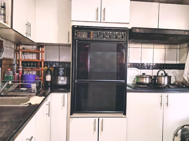 A functional kitchen featuring white built-in cabinetry, a black integrated oven, extractor fan, hob, and tiled backsplash with dark accent tiles.
