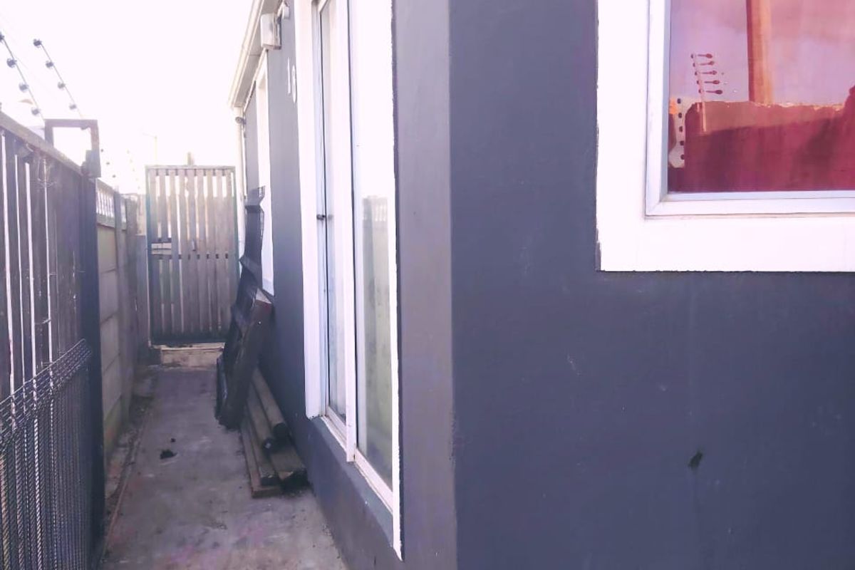 A side exterior view of the property featuring a concrete pathway, electric fencing, and a sliding glass door access point.