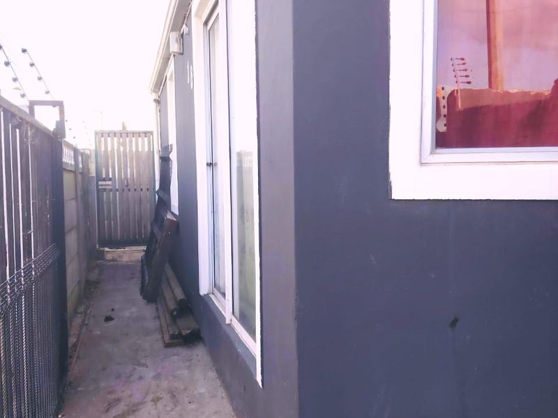 A side exterior view of the property featuring a concrete pathway, electric fencing, and a sliding glass door access point.
