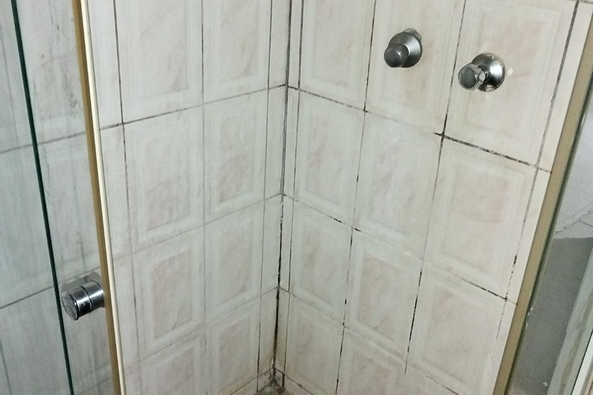 A shower stall featuring tiled walls and flooring with integrated shower mixer and glass enclosure, requiring maintenance and cosmetic updates.