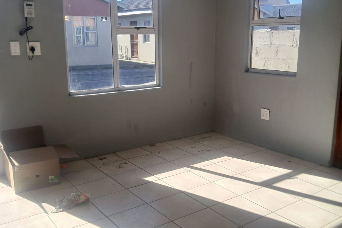 An empty living room featuring tiled flooring, aluminium window frames, and a wall-mounted prepaid electricity meter.