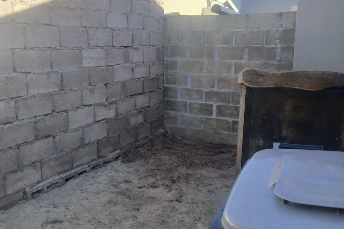 A small, unfinished rear outdoor area featuring exposed concrete block boundary walls and an unpaved ground surface.