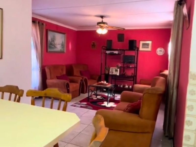 Open plan living and dining area featuring tiled flooring and a ceiling fan, with a vibrant red accent wall.