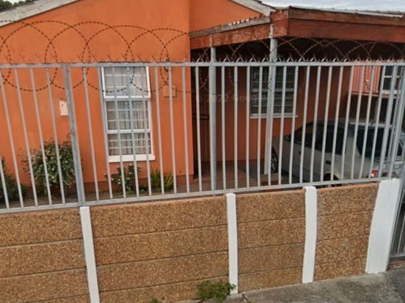 Front elevation of a single-story house featuring a precast concrete boundary wall, metal security fencing with razor wire, and a covered entrance porch.
