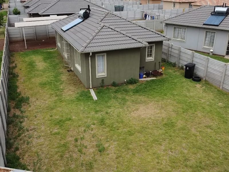 Aerial view of a detached house featuring a tiled roof with a solar water heater, a large grass yard, and precast concrete boundary walls.