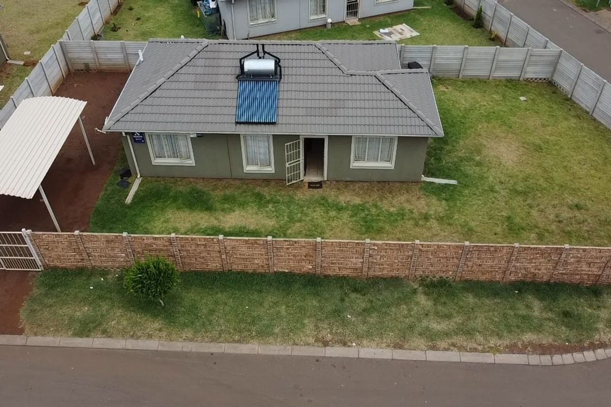 Aerial view of a detached house featuring a tiled roof with a solar water heater, a carport, and a fully fenced yard.