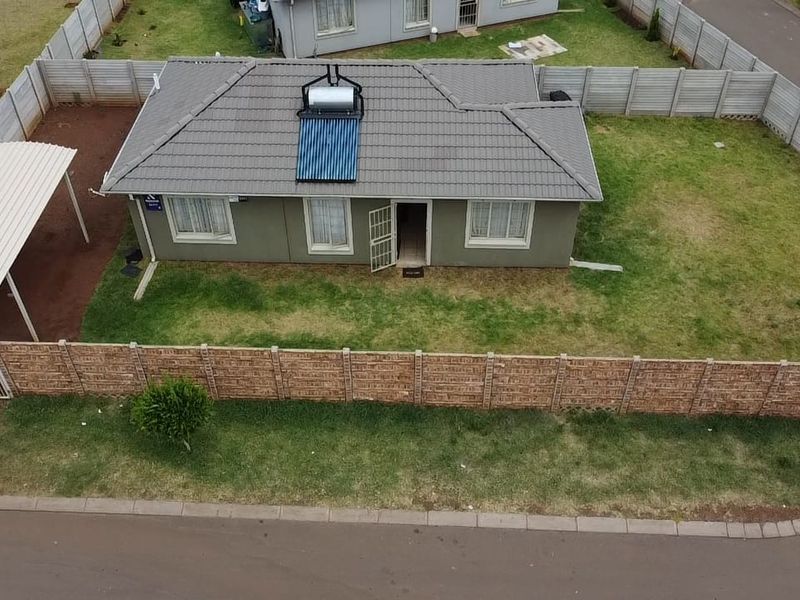 Aerial view of a detached house featuring a tiled roof with a solar water heater, a carport, and a fully fenced yard.