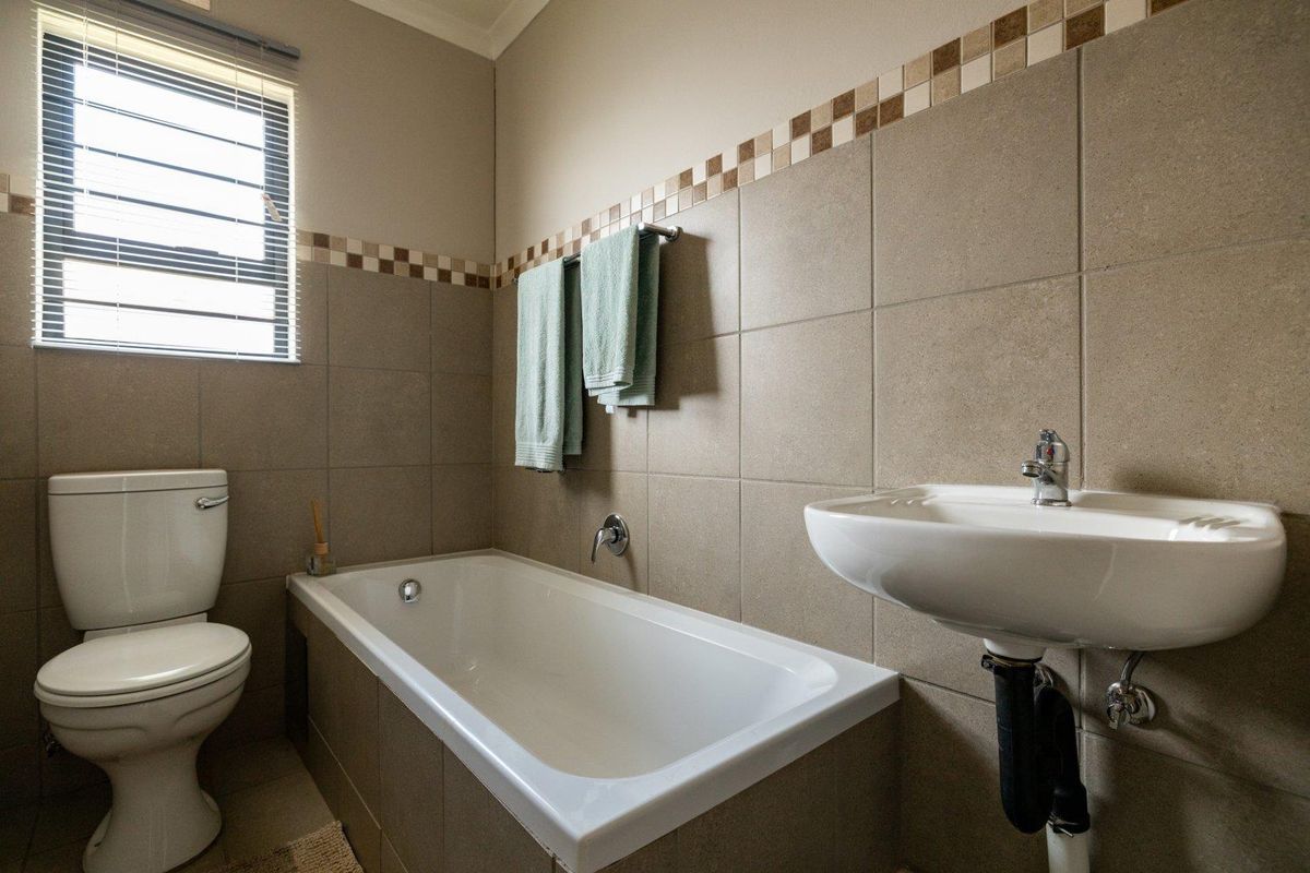 A functional bathroom featuring a bathtub, wall-mounted basin, and toilet with neutral wall tiling and a window for natural light.