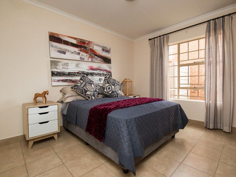 A well-maintained bedroom featuring tiled flooring, a built-in cupboard, and a window fitted with security burglar bars.