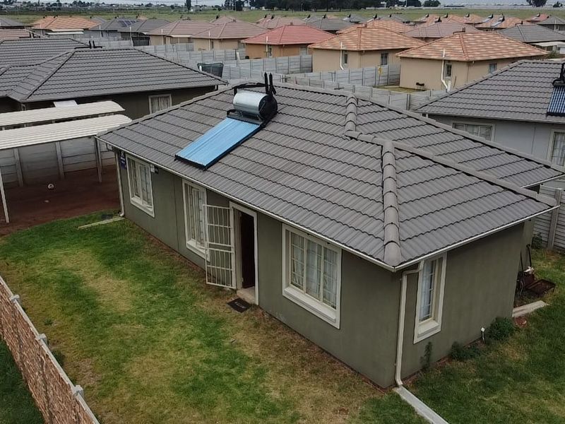 Aerial view of a residential property featuring a tiled roof with a solar water heater, a private garden, and a carport within a fenced yard.