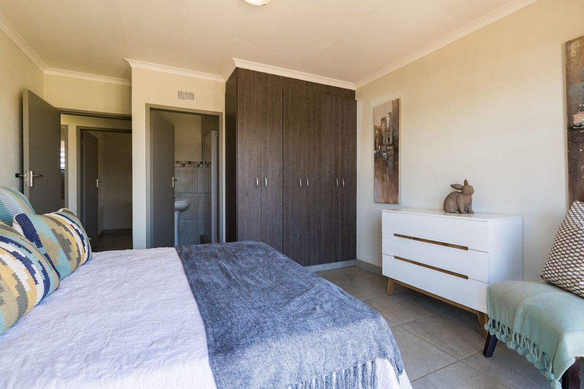A well-maintained bedroom featuring built-in dark wood cupboards, neutral tiled flooring, and direct access to an en-suite bathroom.