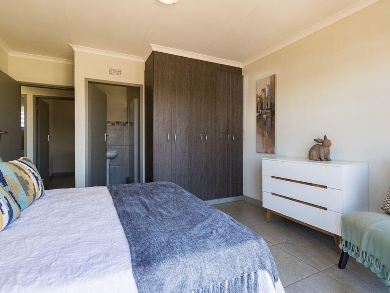 A well-maintained bedroom featuring built-in dark wood cupboards, neutral tiled flooring, and direct access to an en-suite bathroom.