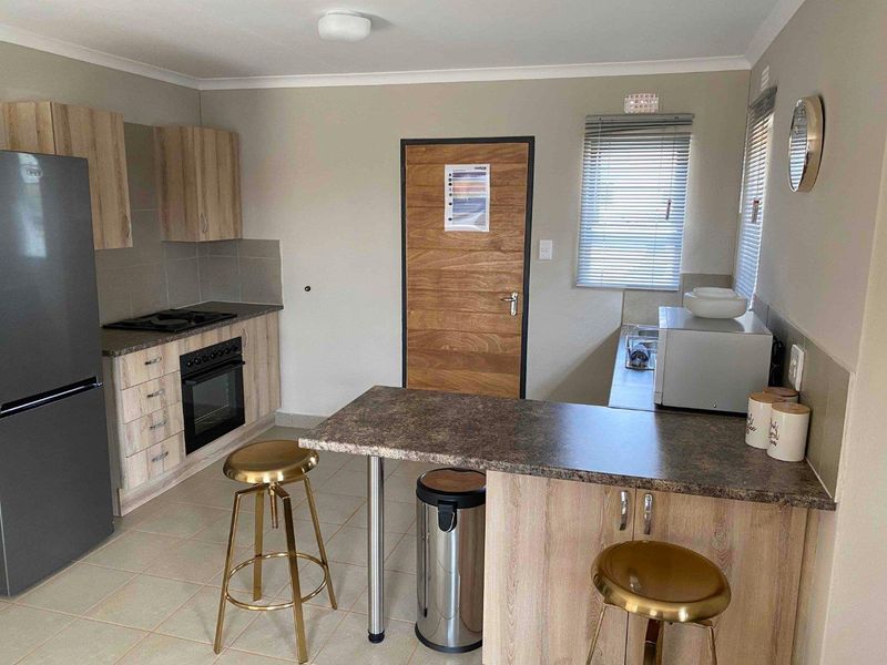 A functional kitchen featuring light wood-look cabinetry, laminate countertops, a built-in oven with gas hob, and tiled flooring.