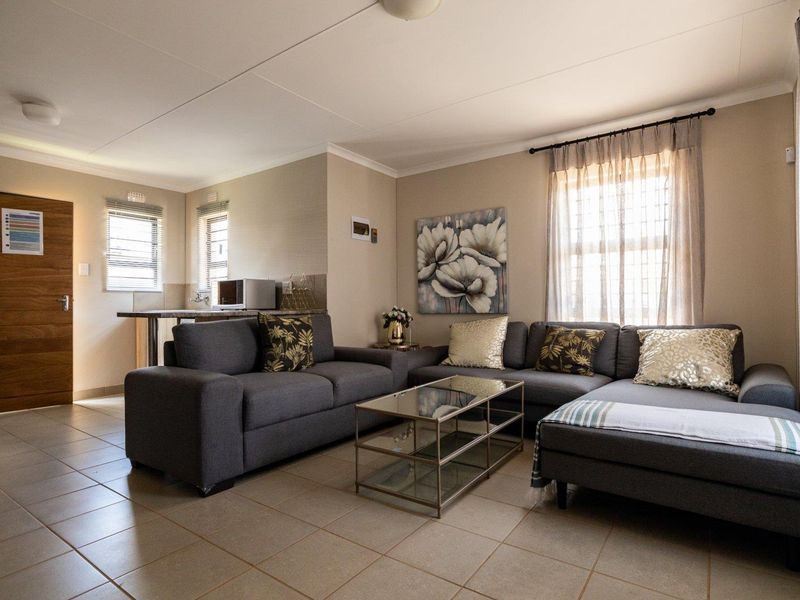 An open-plan living area featuring tiled flooring, neutral wall tones, and a functional kitchen counter space with natural light from multiple windows.