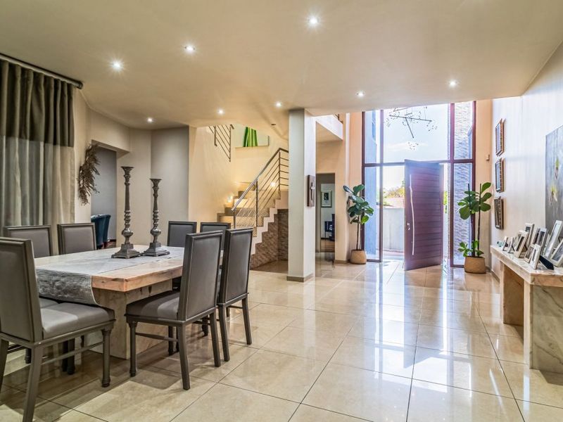 Spacious double-volume entrance hall featuring polished porcelain tiles, a modern staircase with metal balustrades, and a grand pivot front door.