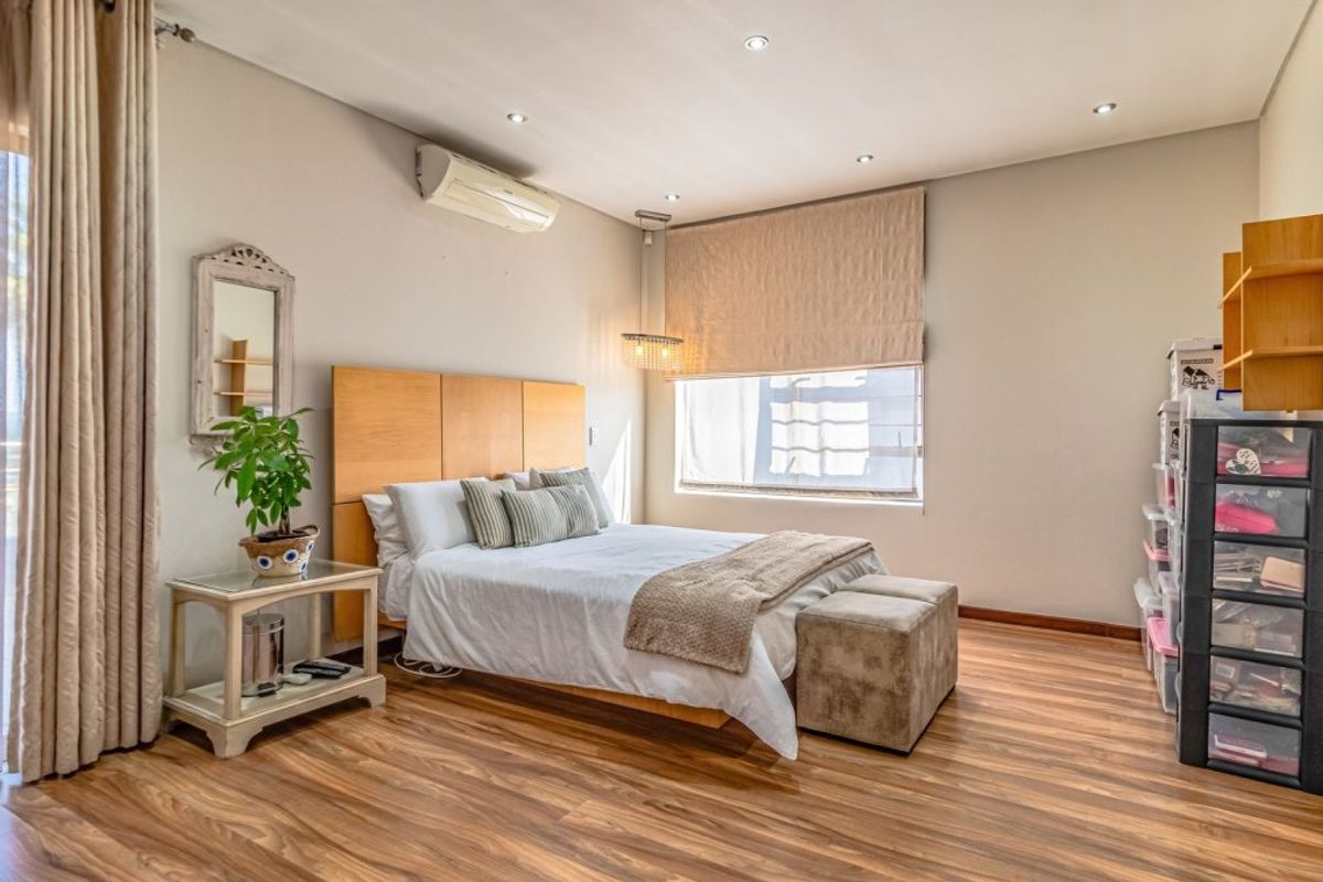 Spacious bedroom featuring warm-toned laminate flooring, recessed lighting, a split-system air conditioner, and direct access to an outdoor area via sliding glass doors.