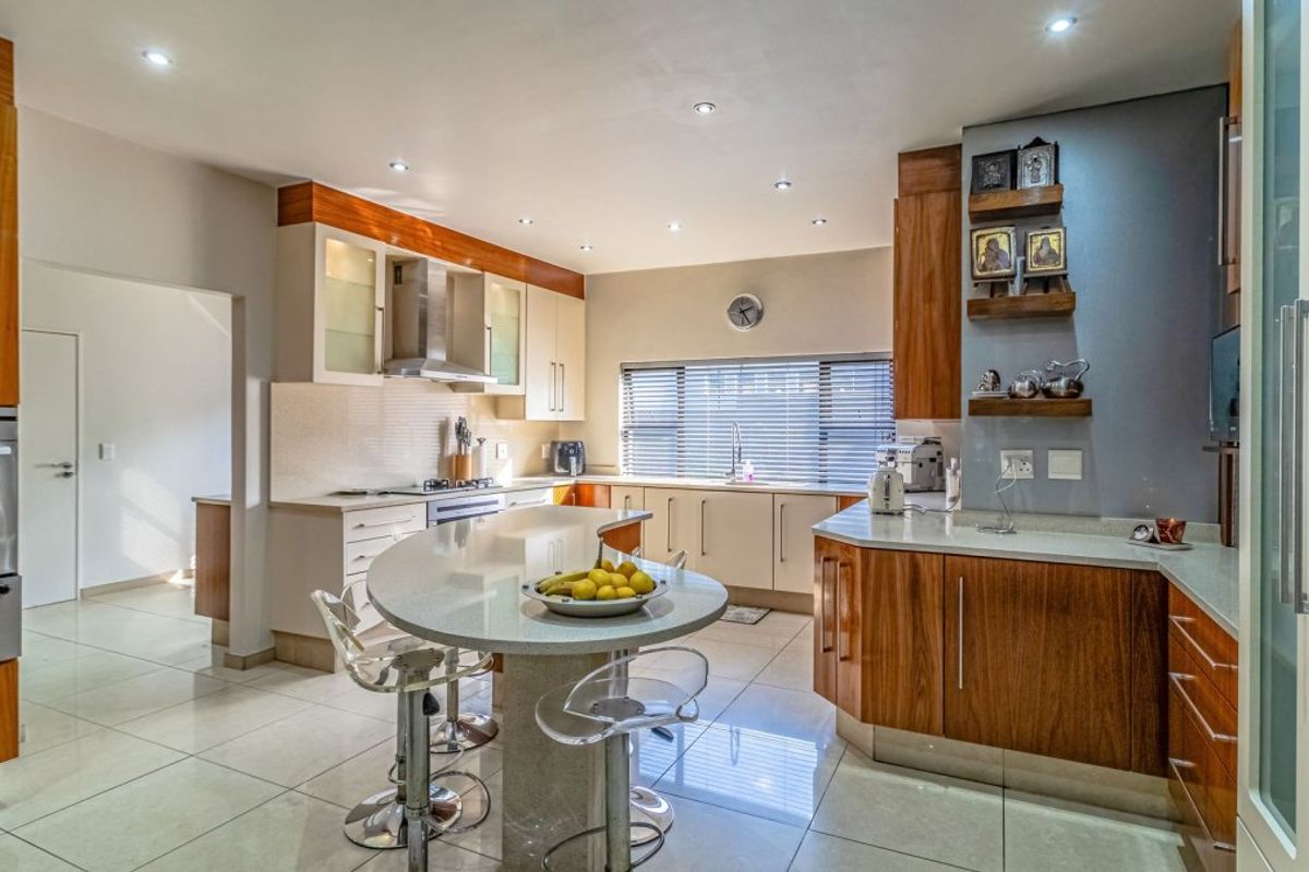 Modern kitchen featuring wood and cream cabinetry, stone countertops, a central breakfast island, built-in oven, and recessed lighting throughout.