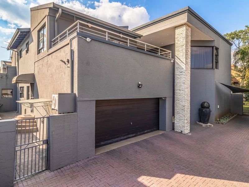 Modern double-storey home exterior featuring a paved driveway, integrated garage, and an upper-level balcony with contemporary stone cladding accents.