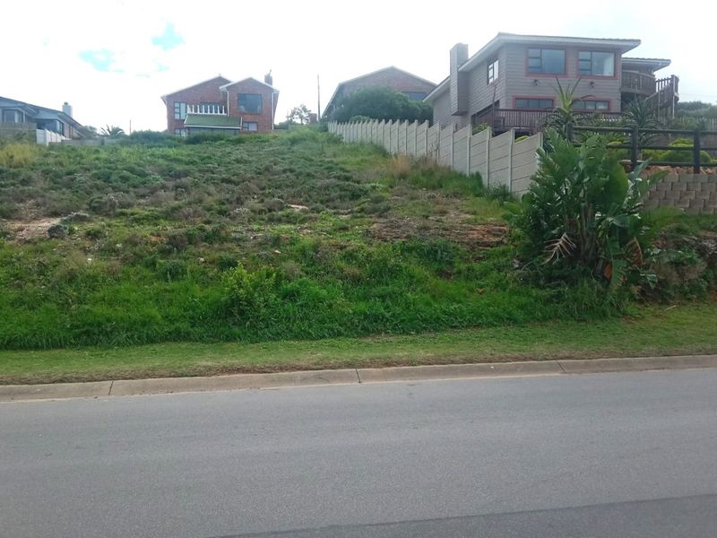 A vacant residential plot with a sloped profile, featuring an existing precast concrete boundary wall and direct access from the paved street.