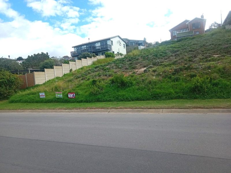 A sloped vacant residential plot viewed from the street, featuring a retaining wall and established ground cover.