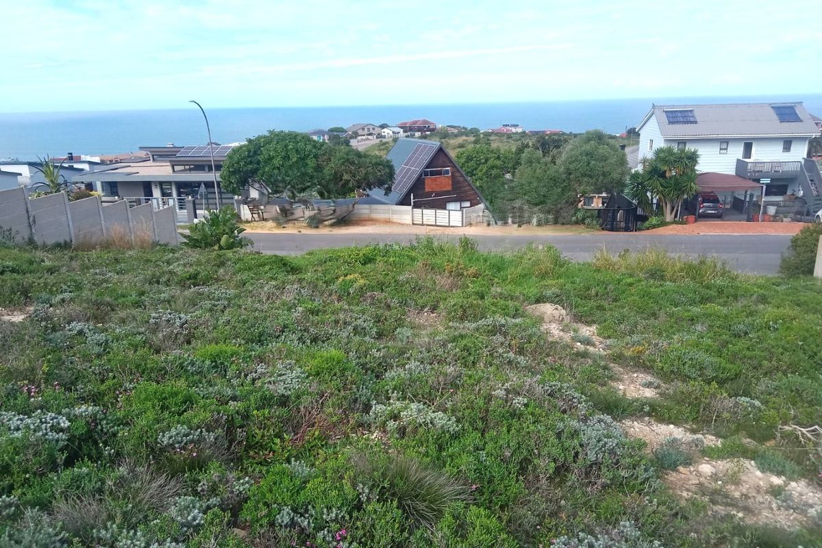 A view overlooking a residential neighborhood with coastal scenery in the background, captured from an elevated vacant land plot.