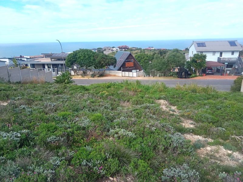 A view overlooking a residential neighborhood with coastal scenery in the background, captured from an elevated vacant land plot.