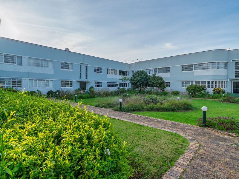 A view of the rear apartment building facade featuring a landscaped garden and a brick paved pathway leading through the communal outdoor space.