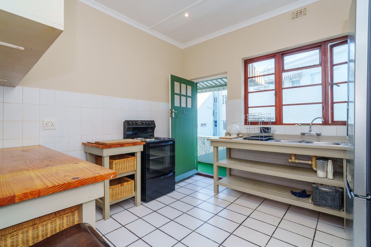 A functional kitchen featuring tiled flooring, a freestanding stove, stainless steel sink, and open shelving with direct access to an outdoor area.