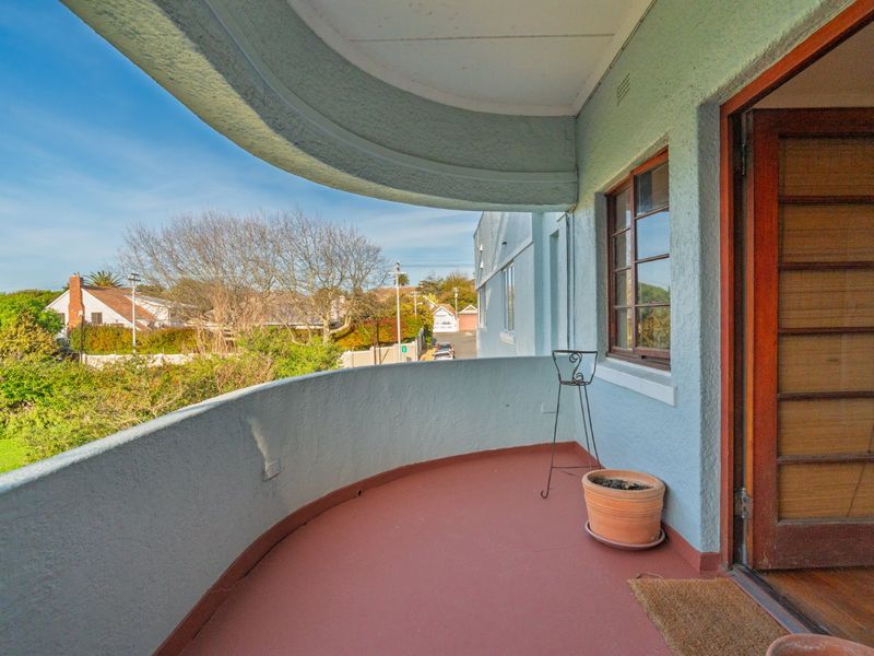 A curved balcony with a painted floor, featuring a timber door and window, offering an elevated view of the surrounding neighborhood.