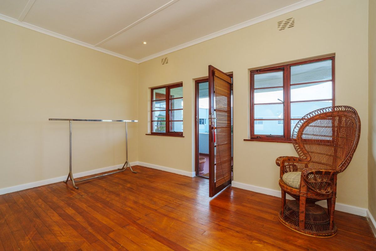 A bright bedroom featuring polished hardwood flooring, timber-framed windows, and direct access to an outdoor balcony area.