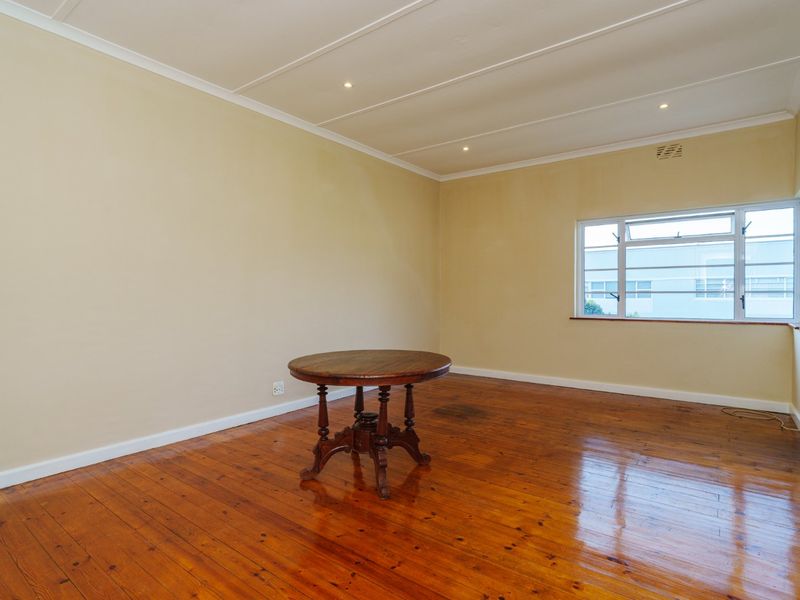 A spacious living area featuring polished hardwood flooring, recessed ceiling lighting, and a large casement window providing natural light.