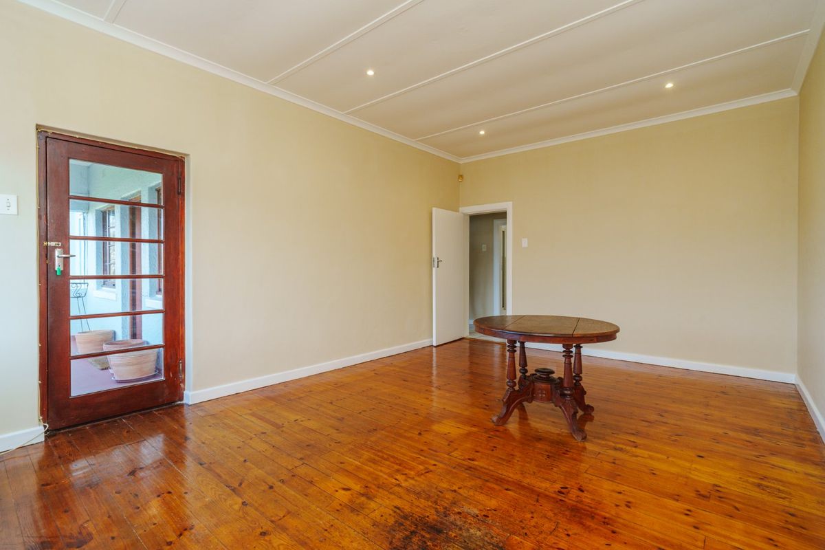 Spacious living area featuring polished hardwood flooring, recessed ceiling lighting, and a timber-framed glass door leading to an outdoor space.