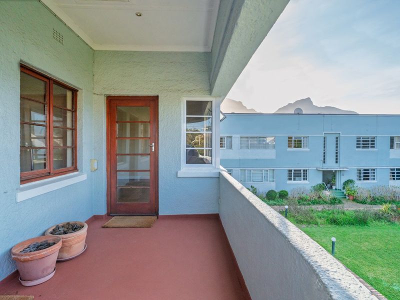 A covered balcony featuring timber-framed windows and doors, overlooking a communal garden area with mountain views.