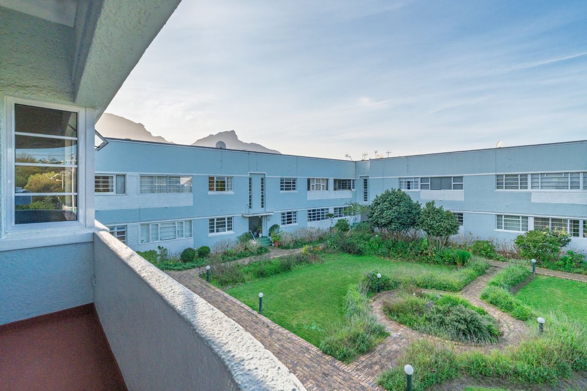 View from a balcony overlooking a communal garden and the rear facade of the apartment complex with mountain views in the distance.