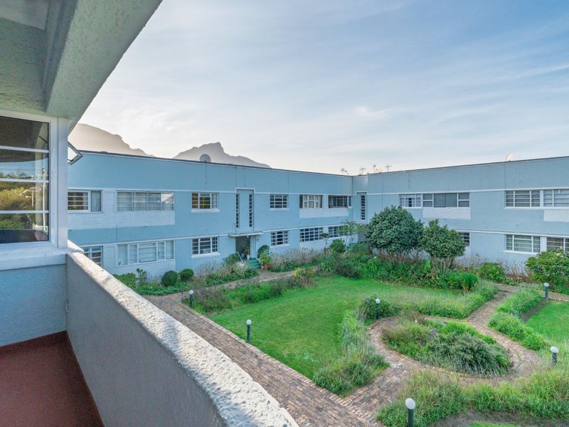 View from a balcony overlooking a communal garden and the rear facade of the apartment complex with mountain views in the distance.