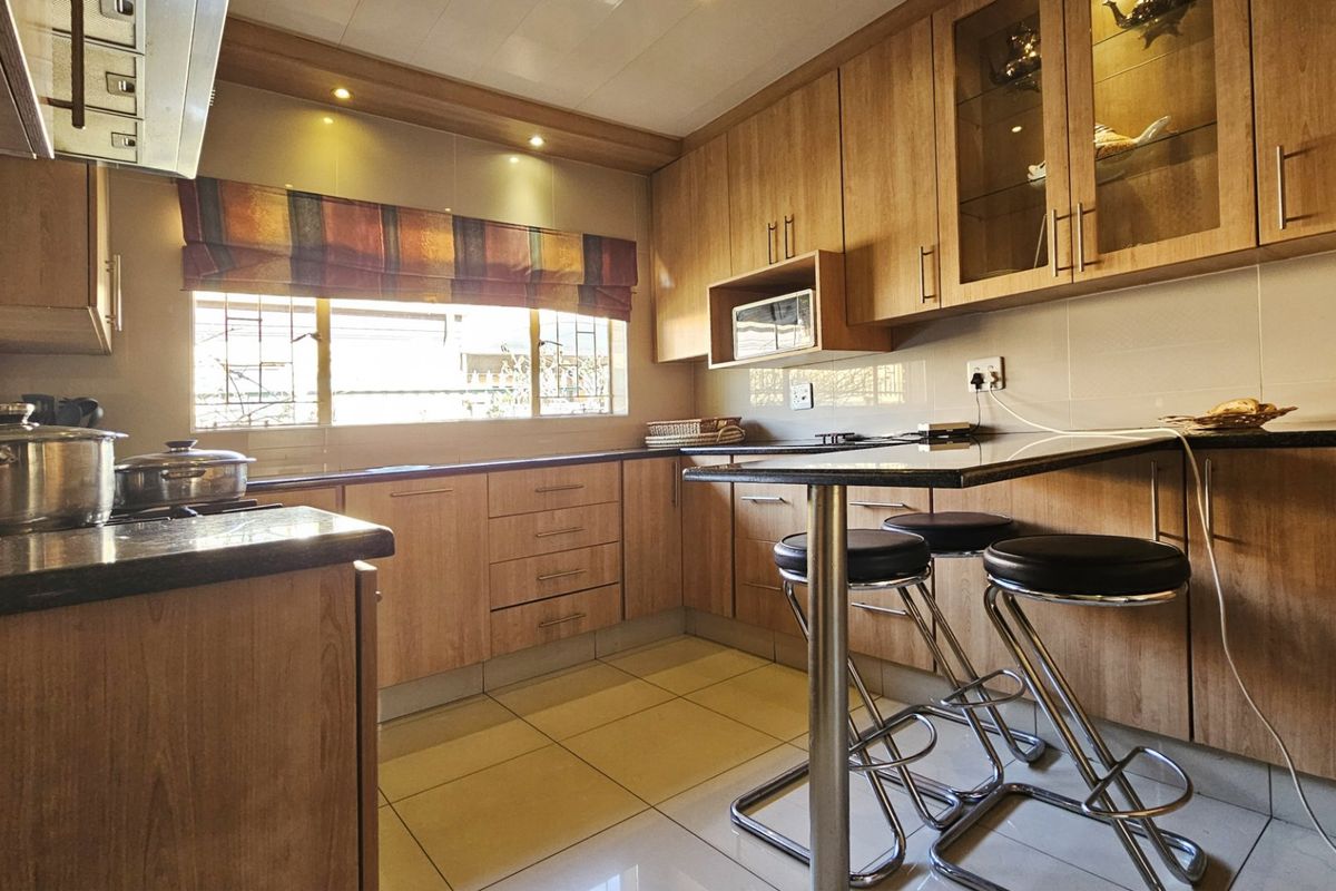 A functional kitchen featuring wood-finish cabinetry, granite countertops, built-in microwave, extractor fan, and tiled flooring with a breakfast bar area.