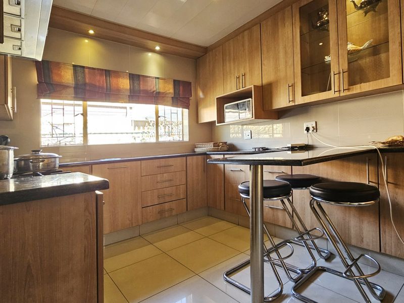 A functional kitchen featuring wood-finish cabinetry, granite countertops, built-in microwave, extractor fan, and tiled flooring with a breakfast bar area.
