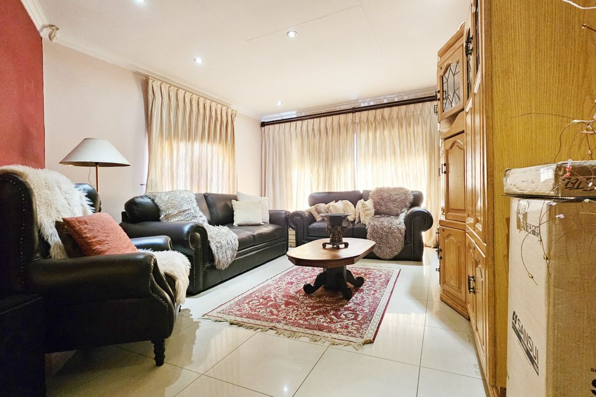 A comfortable living room featuring tiled flooring, recessed downlighting, and large windows dressed with curtains.