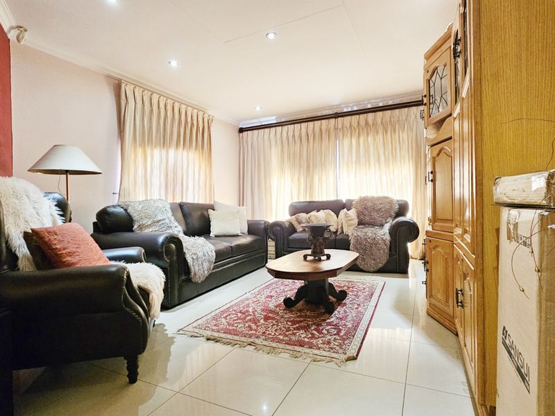 A comfortable living room featuring tiled flooring, recessed downlighting, and large windows dressed with curtains.