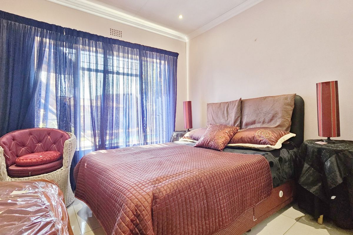 A well-lit bedroom featuring tiled flooring, decorative cornicing, and large windows with curtain rails, providing a comfortable and functional living space.