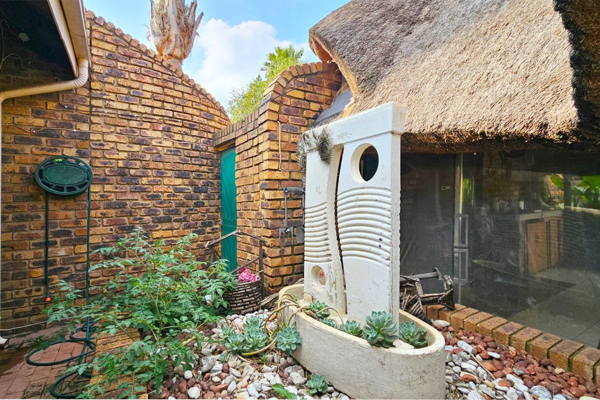 A rear courtyard area featuring face brick walls, a thatched roof section, and a decorative stone water feature set within a pebble garden bed.