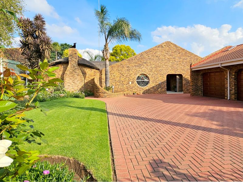 Front elevation of a face brick house featuring a paved driveway, double garage, and a well-maintained garden with a unique circular window design.