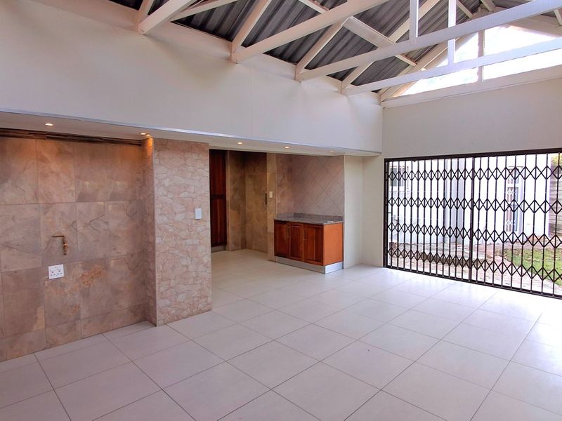 Spacious covered patio featuring exposed roof trusses, a stone-clad feature wall, built-in cabinetry, and large security gate access to the garden.