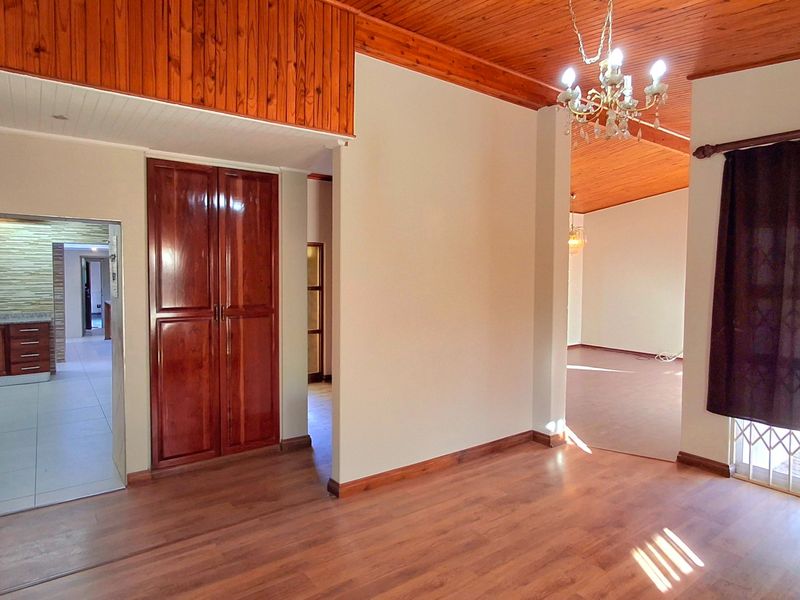 Spacious open-plan living area featuring timber ceilings, laminate flooring, and a built-in cupboard, with a view through to the kitchen area.