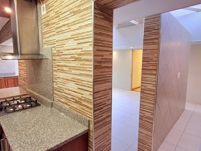 Modern kitchen featuring granite countertops, a gas hob with stainless steel extractor, and decorative wall tiling, leading into an open-plan living area.