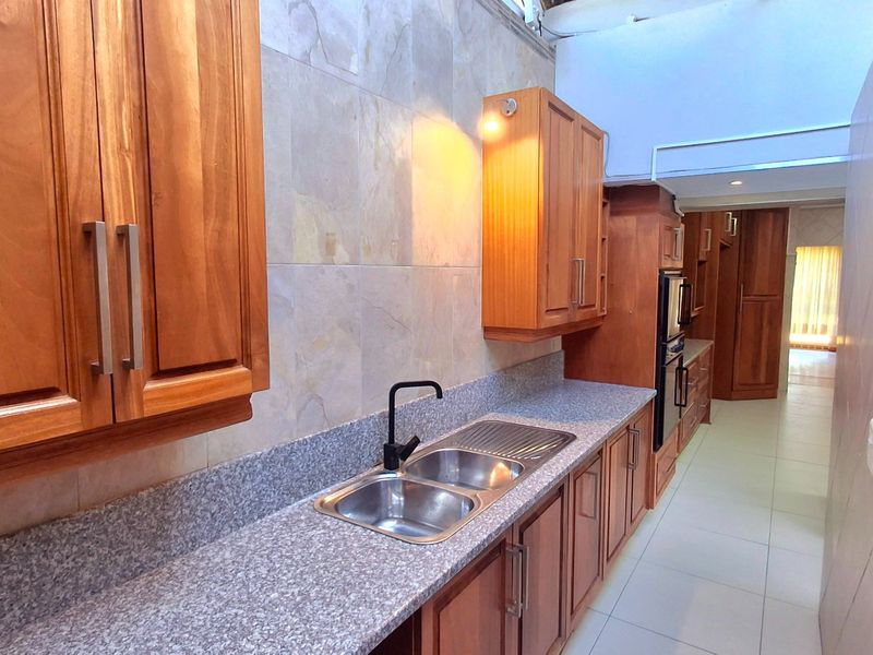 A well-maintained kitchen featuring wooden cabinetry, granite countertops, a double bowl stainless steel sink, and built-in oven, finished with tiled backsplash and flooring.